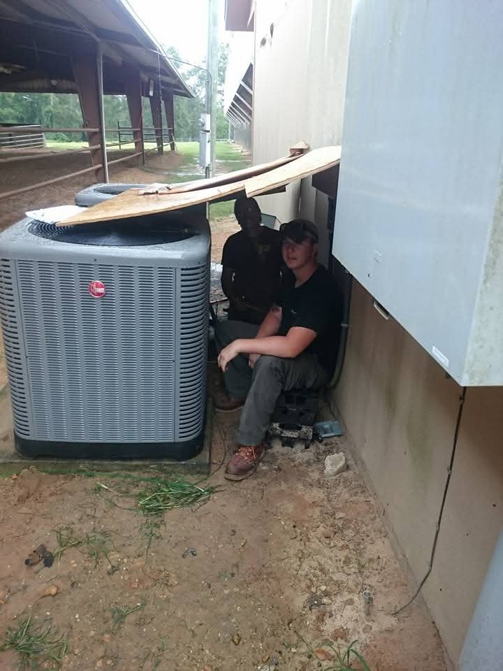 Two techs sheltering in the rain next to Rheem unit