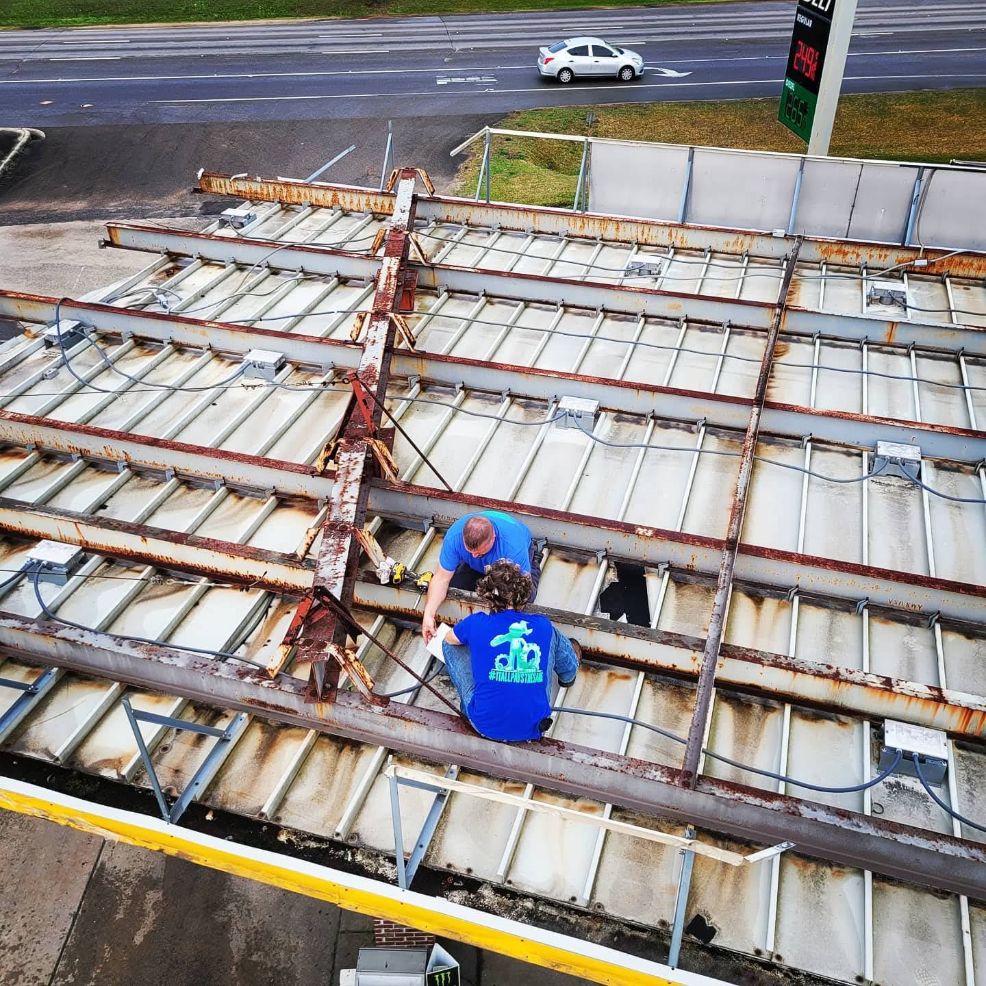 Two techs on rusted canopy top wiring new fixtures